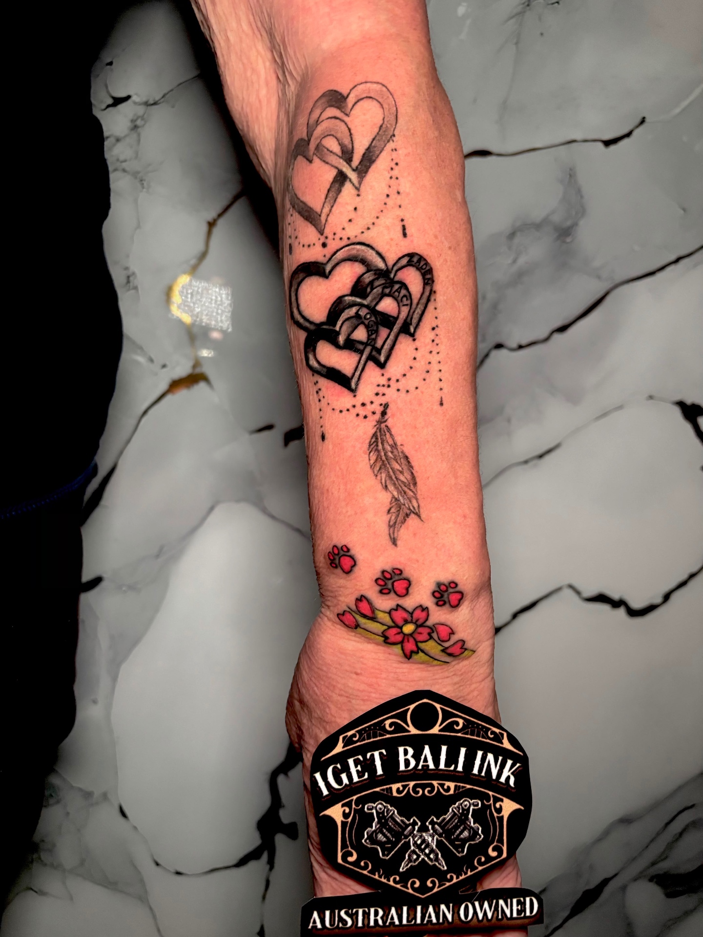 Linked hearts with names, feather and colour paw prints on the forearm
