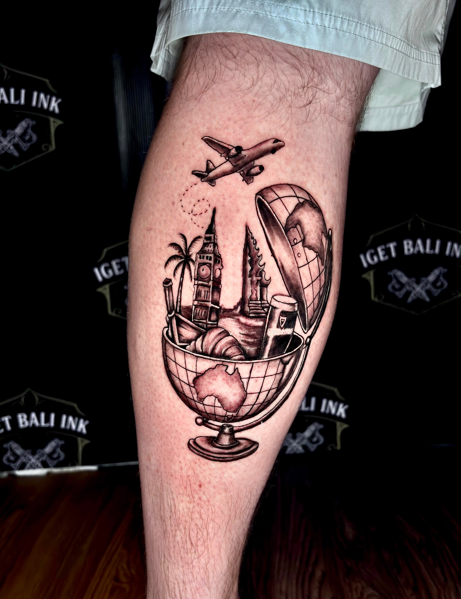Black and grey travel globe, plane and landmarks calf tattoo