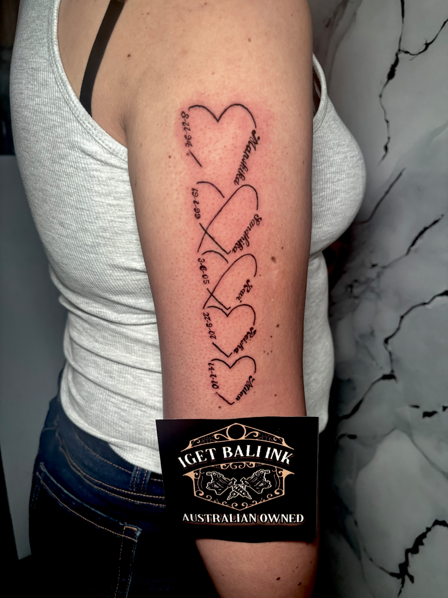 Fine line linked hearts with names and dates on the arm